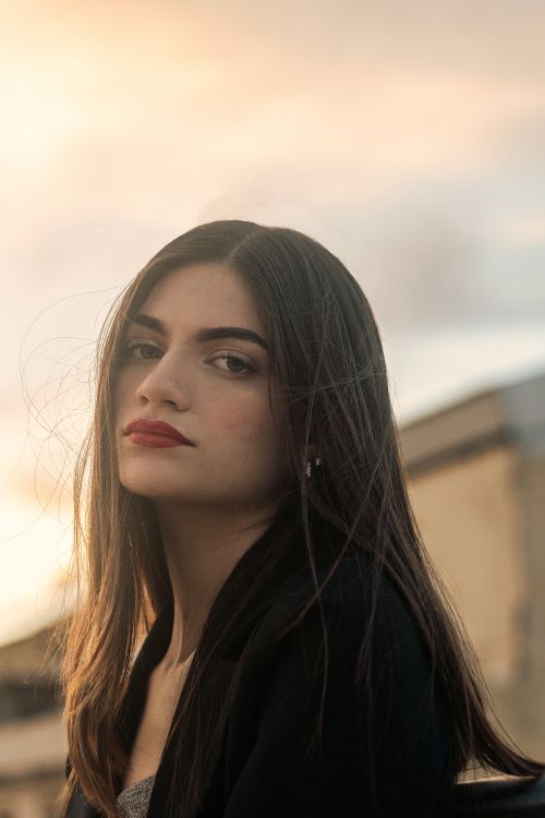 Free Portrait of a young brunette woman with red lips at sunset, exuding elegance. Stock Photo