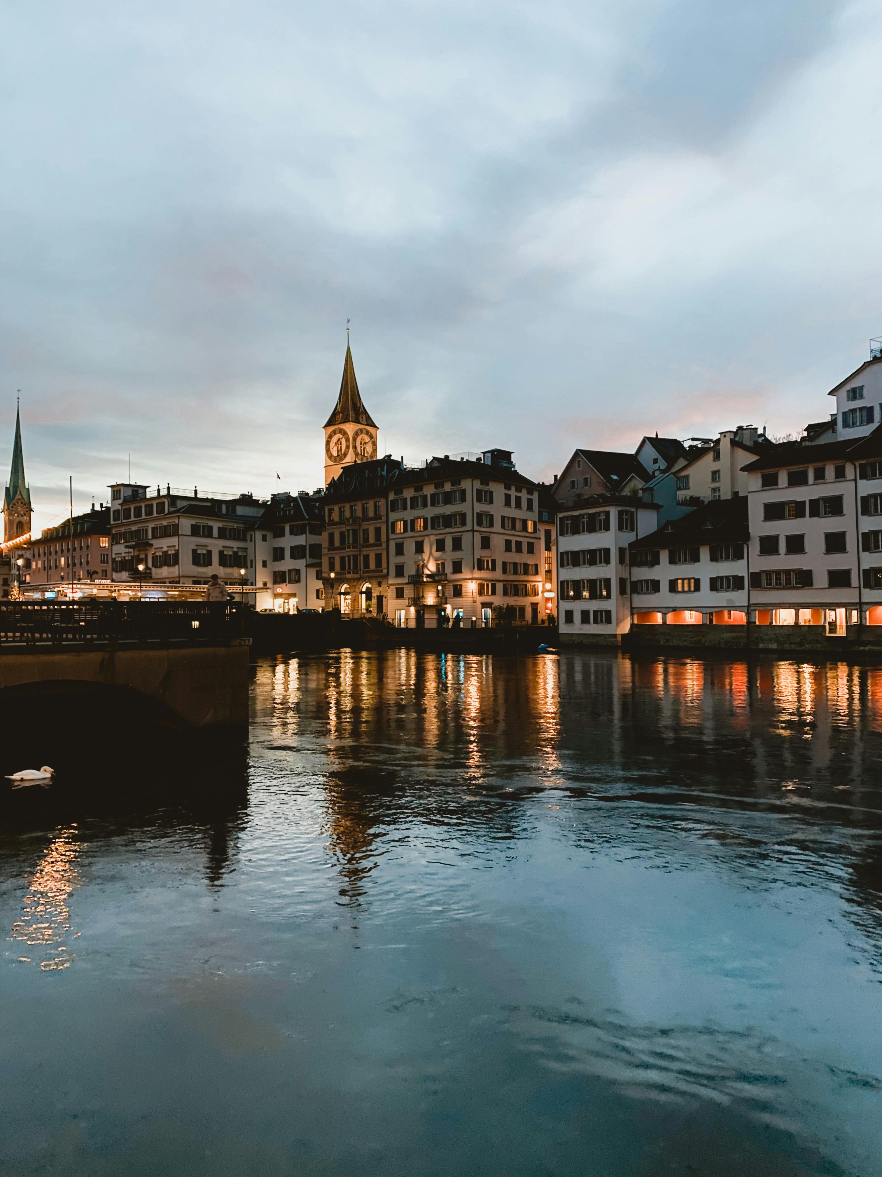 Charming evening view of Zurich's riverfront with illuminated buildings reflecting on the water.