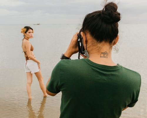 Photographer Taking Photo of Brunette Woman in Bra and Shorts on Beach