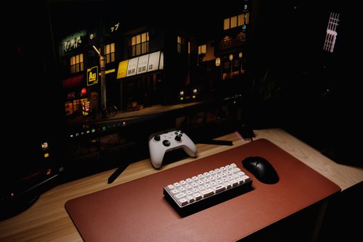 Close-up of a gaming desk setup featuring a keyboard, controller, and monitor at night.