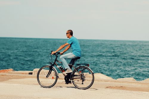 Free A man rides a bicycle along the seashore in Palermo, Sicily, enjoying a sunny day by the ocean. Stock Photo