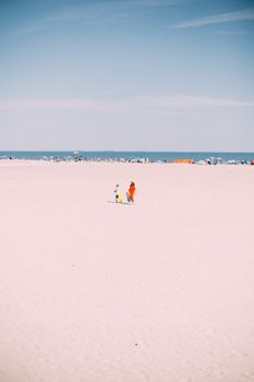 A mother and child stroll along a sunny beach in summer, New York.