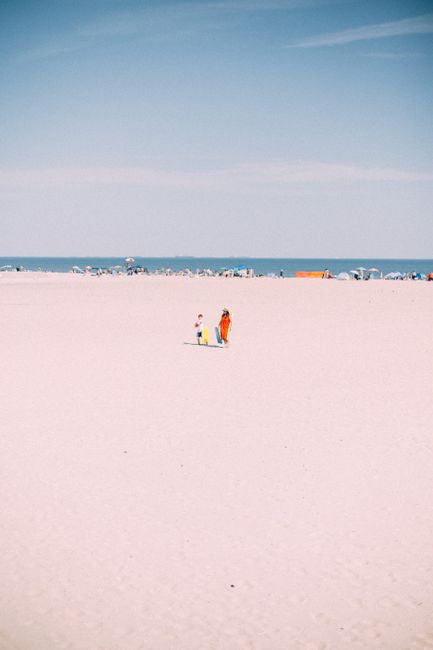A mother and child stroll along a sunny beach in summer, New York.