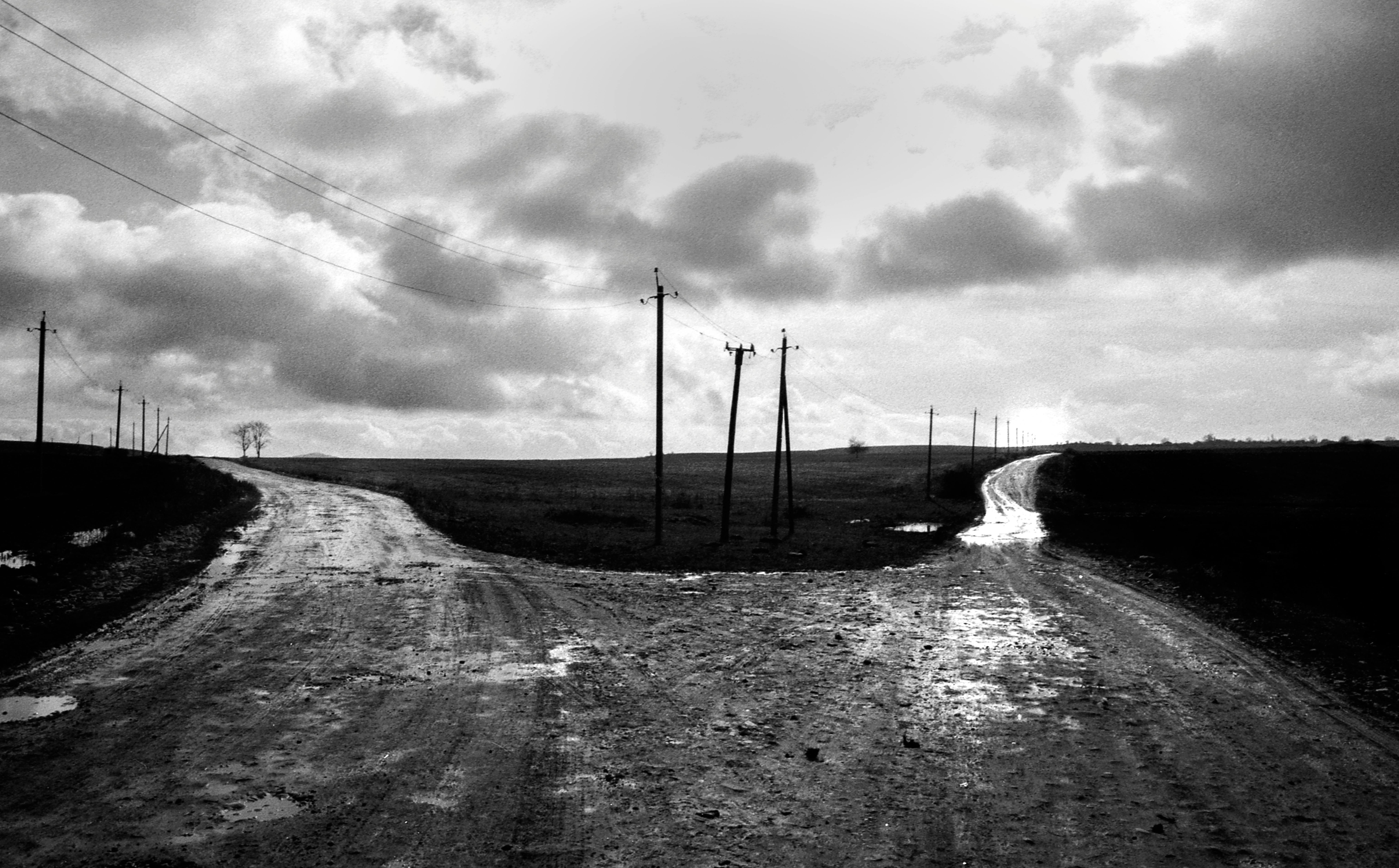 Monochrome image of a rural crossroad with utility poles under a cloudy sky.