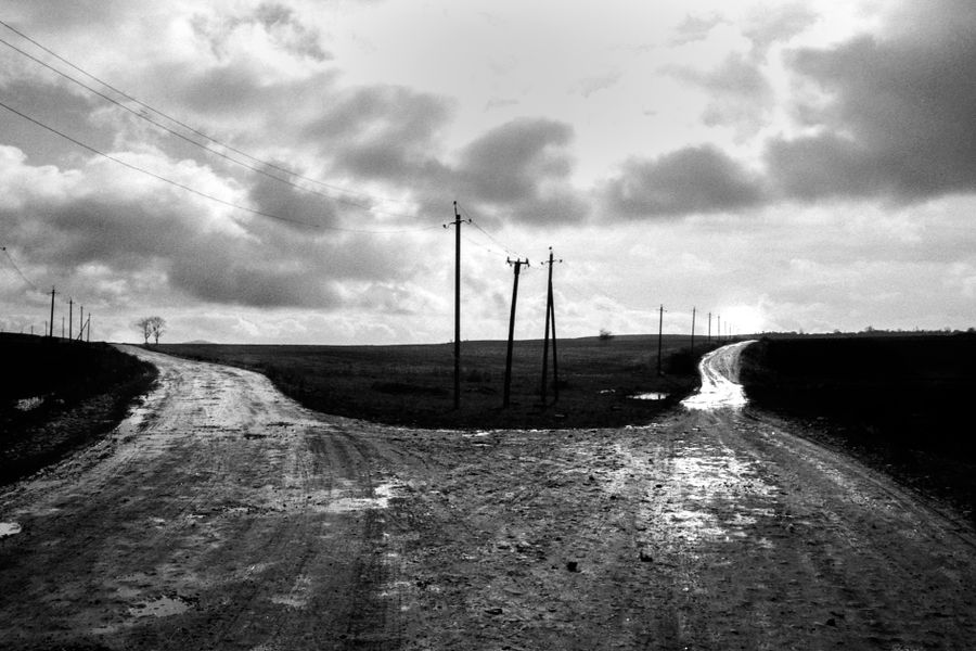 Monochrome image of a rural crossroad with utility poles under a cloudy sky.