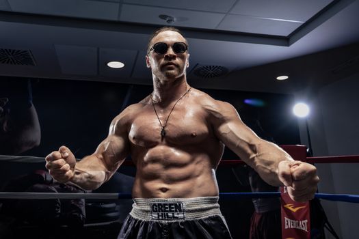 Muscular boxer posing in an indoor boxing ring wearing sunglasses.