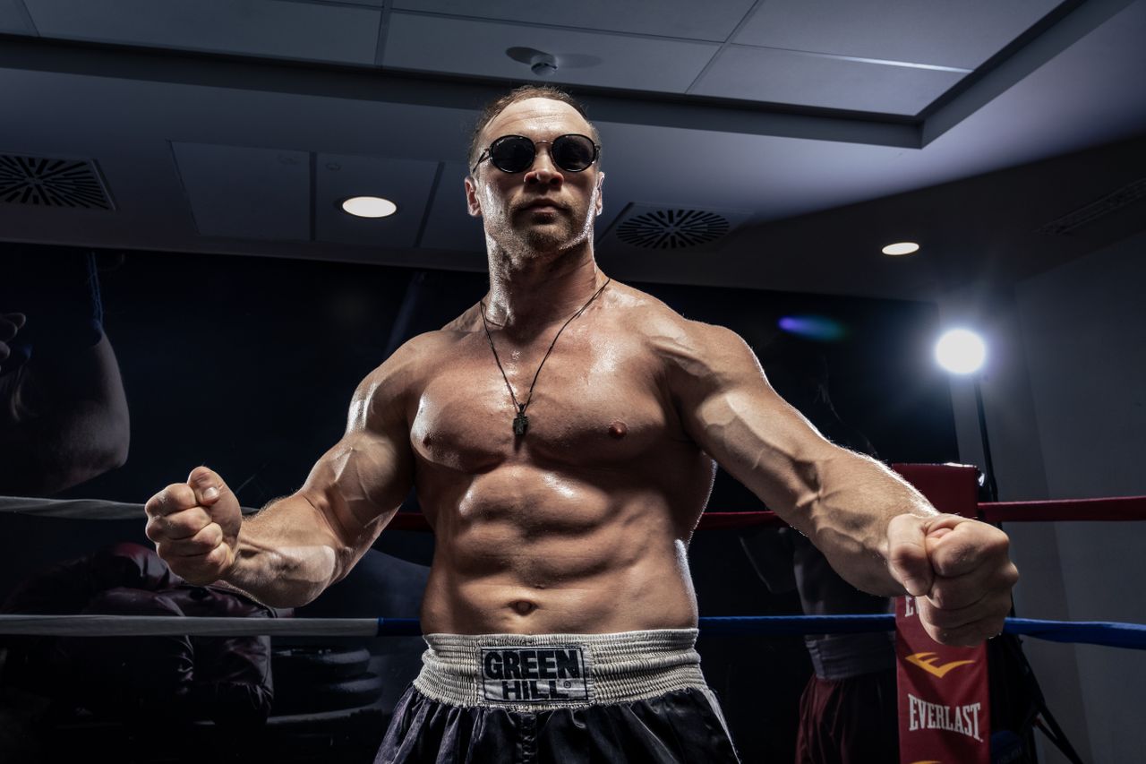 muscular boxer posing in an indoor boxing ring wearing sunglasses