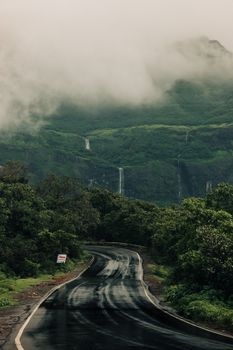 Curving road through misty mountains and lush greenery with visible waterfalls. Ideal for nature enthusiasts.