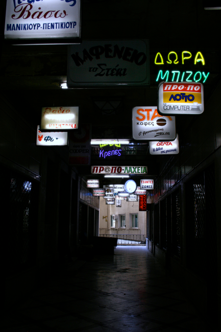 Explore the vibrant neon-lit corridor in Monastiraki, Greece, showcasing diverse shop signs.