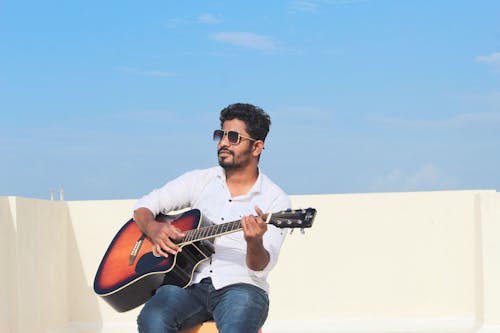 Man in Sunglasses Sitting and Playing Guitar