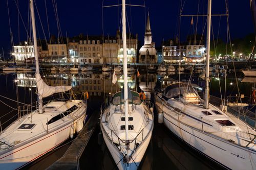 Free Scenic nighttime view of Honfleur marina with illuminated sailboats against a charming urban backdrop. Stock Photo