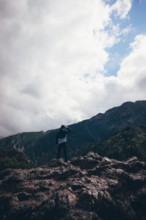 Free Man standing on rocky terrain in Tatra Mountains, Poland, with dramatic cloudy sky. Stock Photo