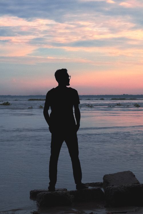 Free Silhouette of a man standing on a rocky shore at sunset in Chandpur, Bangladesh. Stock Photo