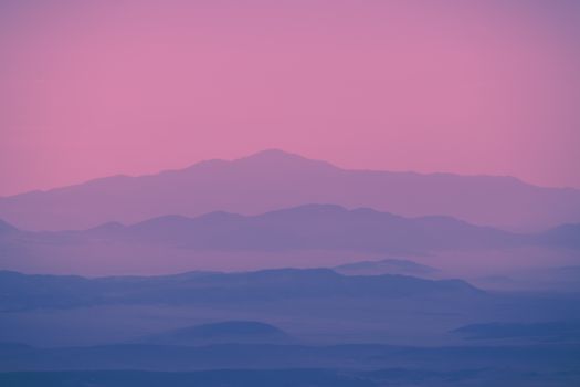 Beautiful layered mountains at twilight featuring soft pink and blue hues, creating a tranquil atmosphere.