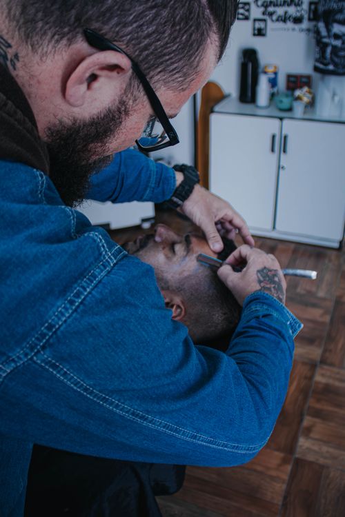 Free Barber skillfully shaves a client's face with a razor in a contemporary barbershop. Stock Photo