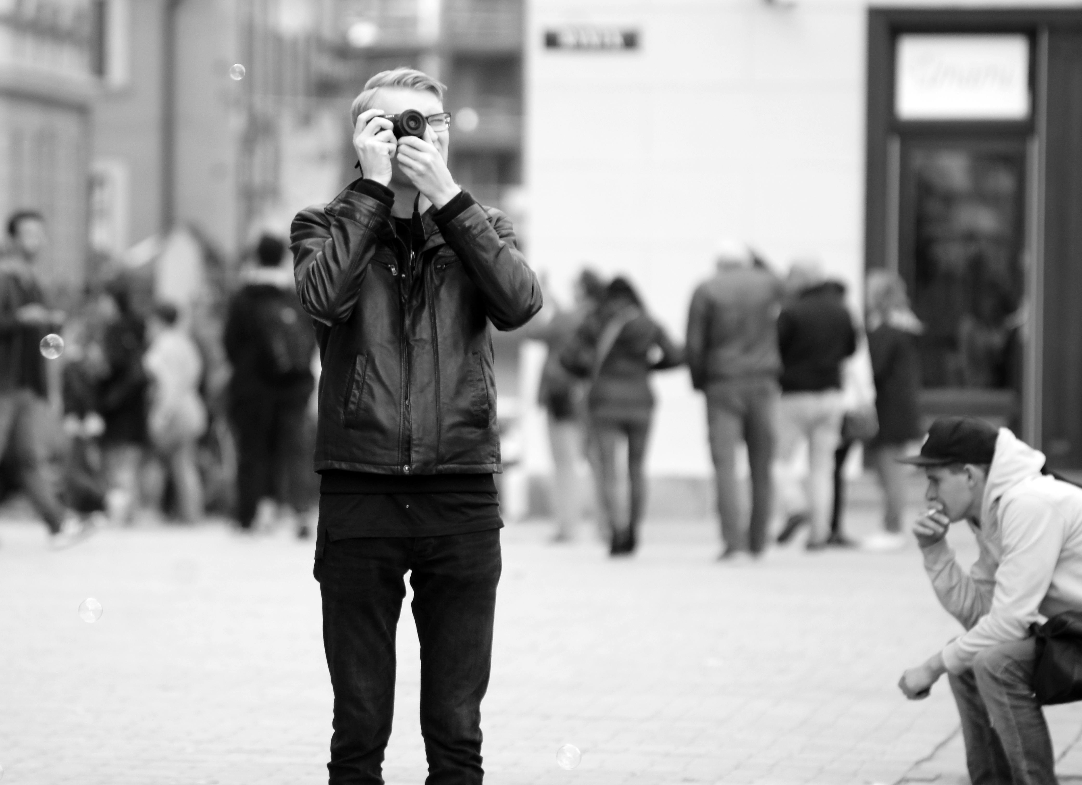 Free A man photographs city streets in black and white amidst a busy urban crowd. Stock Photo