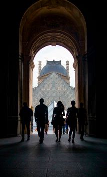 Silhouettes of people walking through an archway at the Louvre, Paris, France.