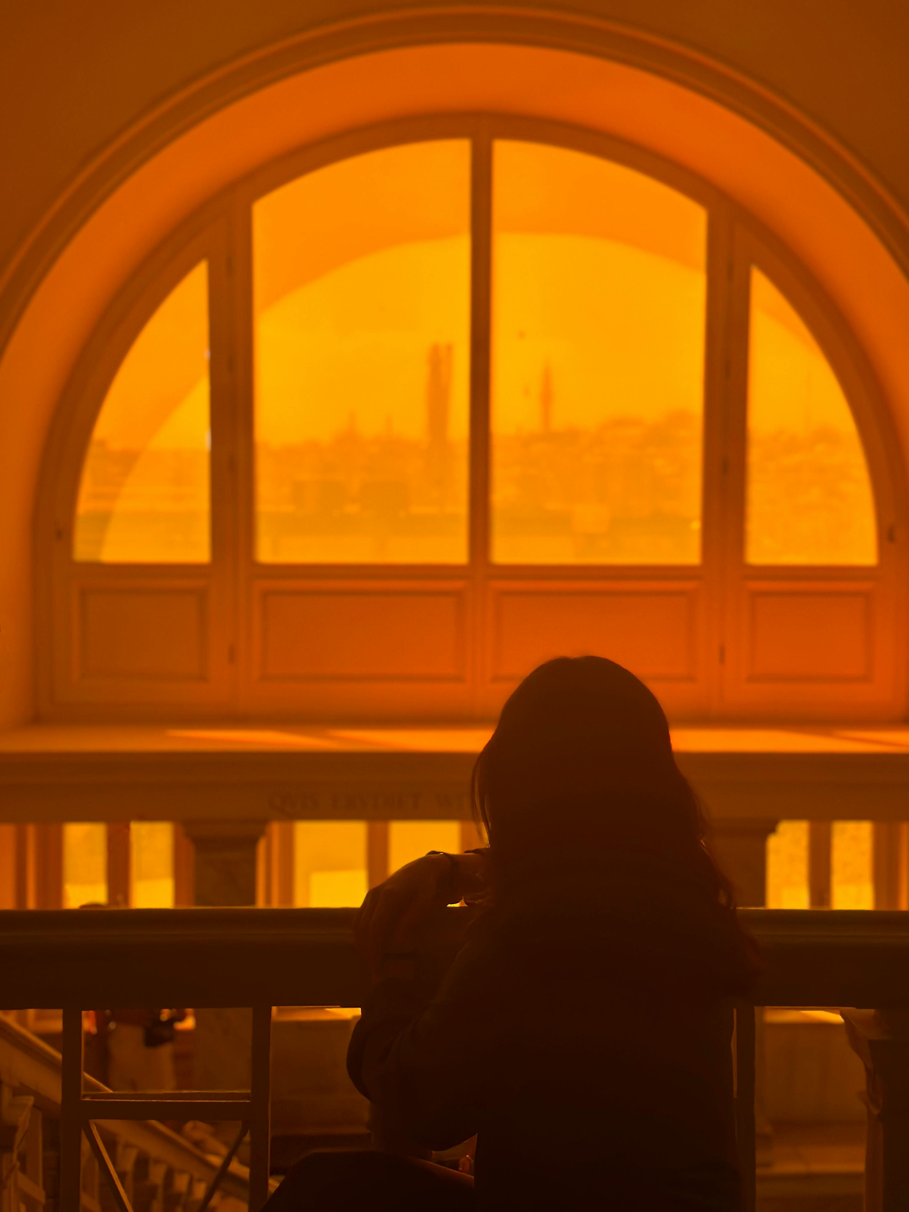 A peaceful silhouette of a person looking out an arched window during a vibrant sunset.