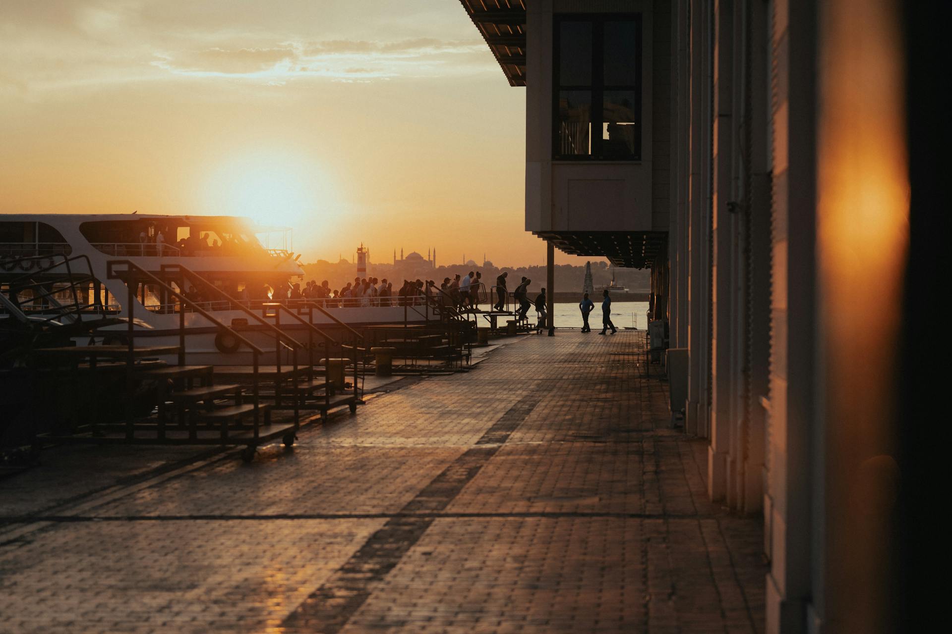 Silhouettes of people and ferry at a waterfront terminal in Istanbul during sunset.
