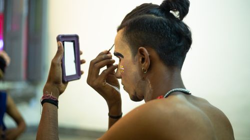 Free A man uses a mirror to apply traditional face paint indoors, reflecting cultural artistry and diversity. Stock Photo