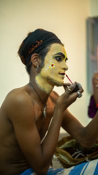 A man applies artistic face paint in preparation for a traditional Indian festival.