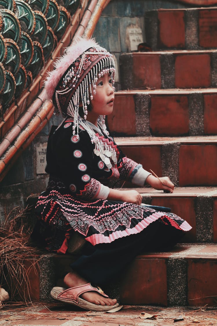 Little Child In Hmong Folk Costume Sitting On The Stairs