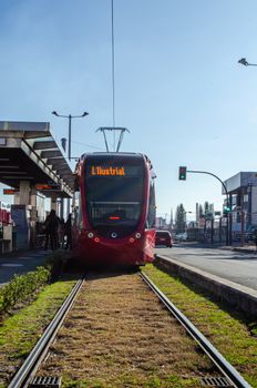 Red tram at a tram stop in Cuenca, Ecuador with a clear sky and urban backdrop.