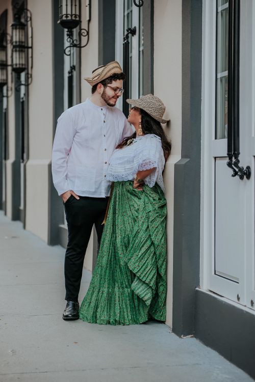 Free A loving couple in stylish hats lean against a city facade, smiling warmly. Stock Photo