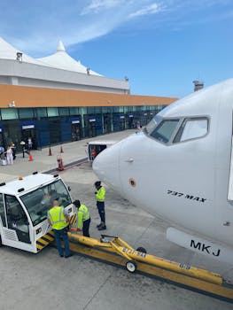 Boeing 737 MAX aircraft at airport terminal with ground crew preparing for flight.