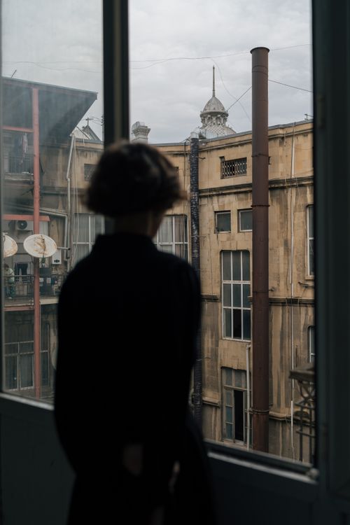 Free A silhouette of a woman gazing at Baku's unique architectural style through a window, evoking solitude. Stock Photo