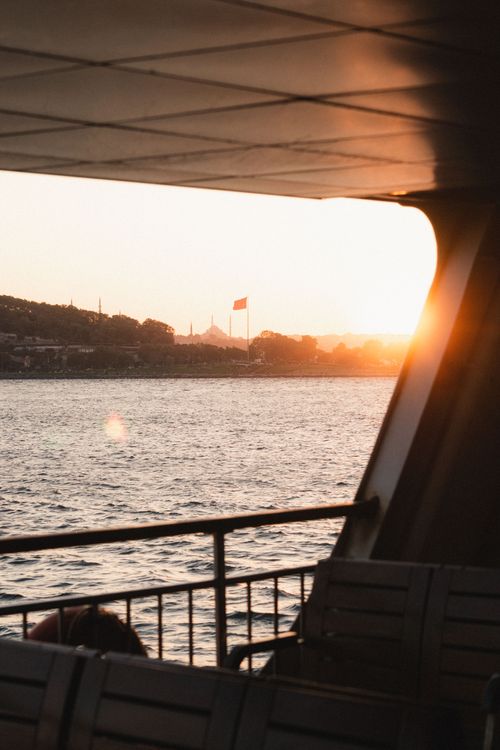 Free A serene view from a ferry at sunrise overlooking the coastline and distant flag. Stock Photo