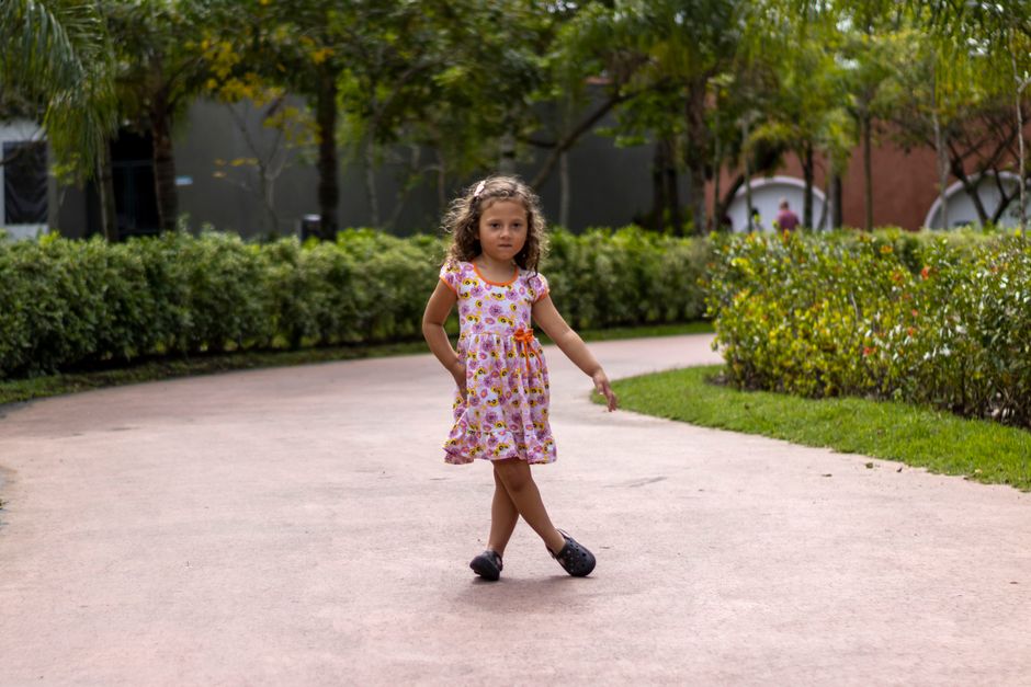 Young girl in a floral dress walking confidently in a park at Praia Grande, Brazil.