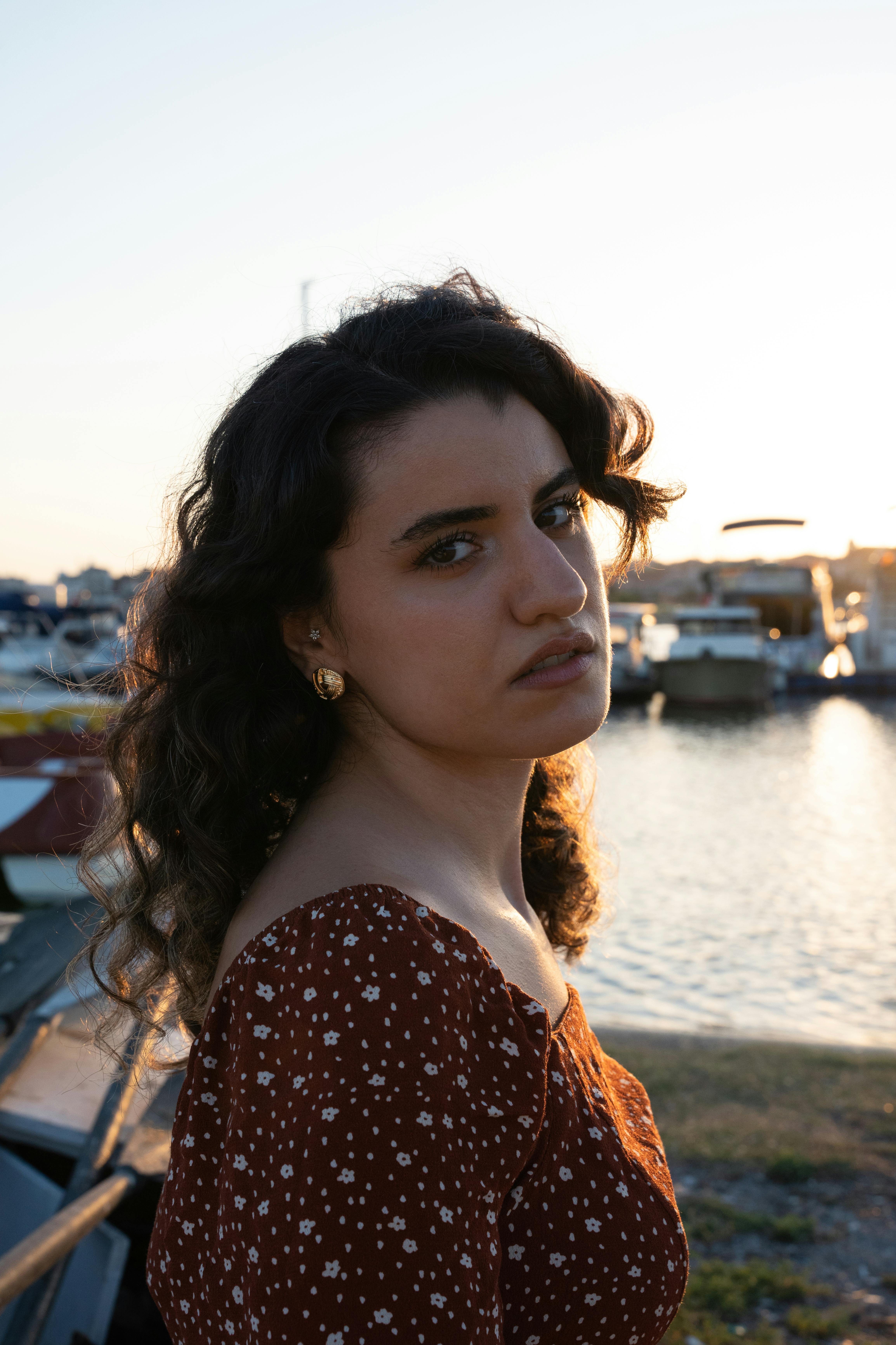 A young woman stands by the marina at sunset, embracing a serene summer evening.