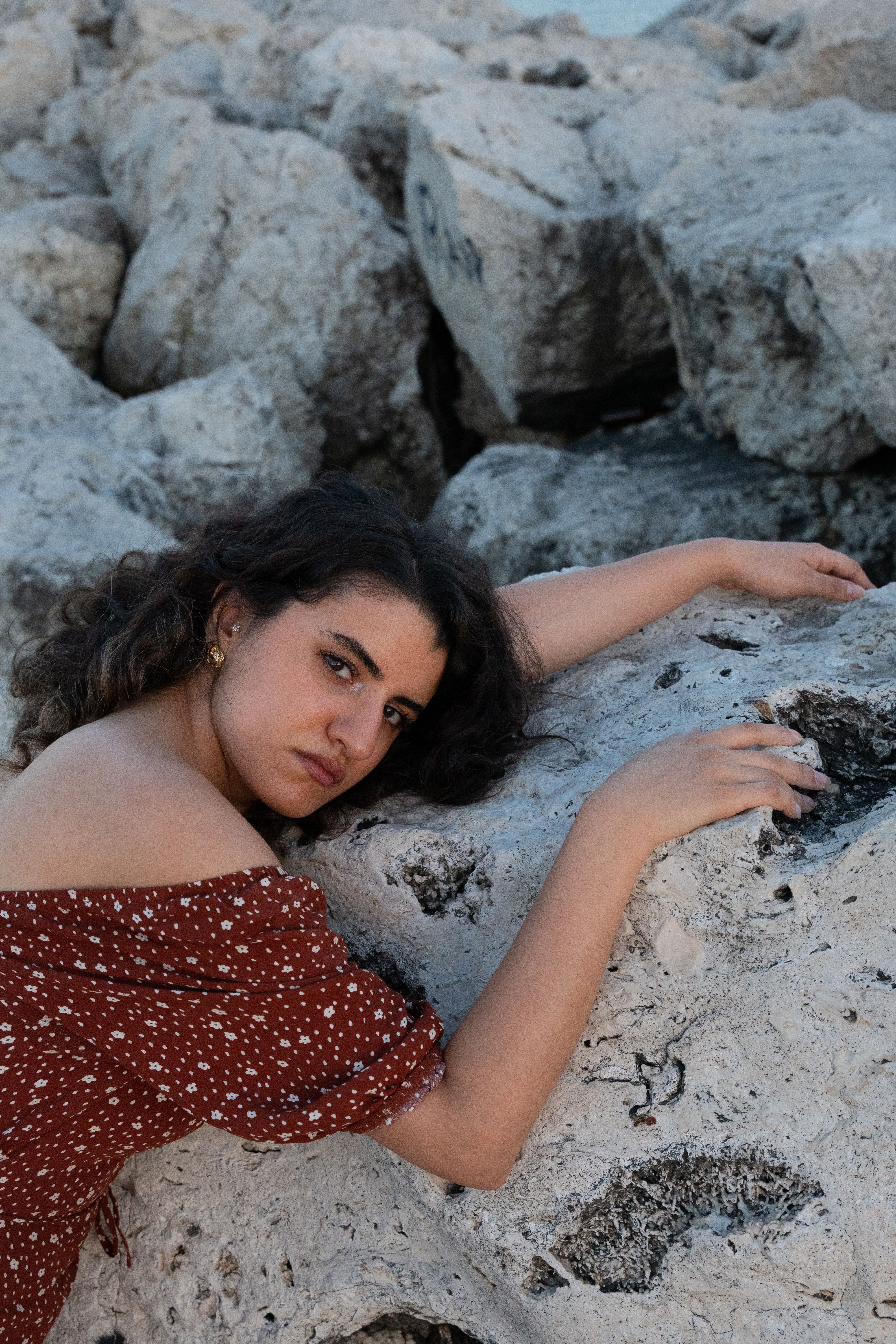 A young woman in a stylish dress poses gracefully on a rocky beach, making a fashion statement.