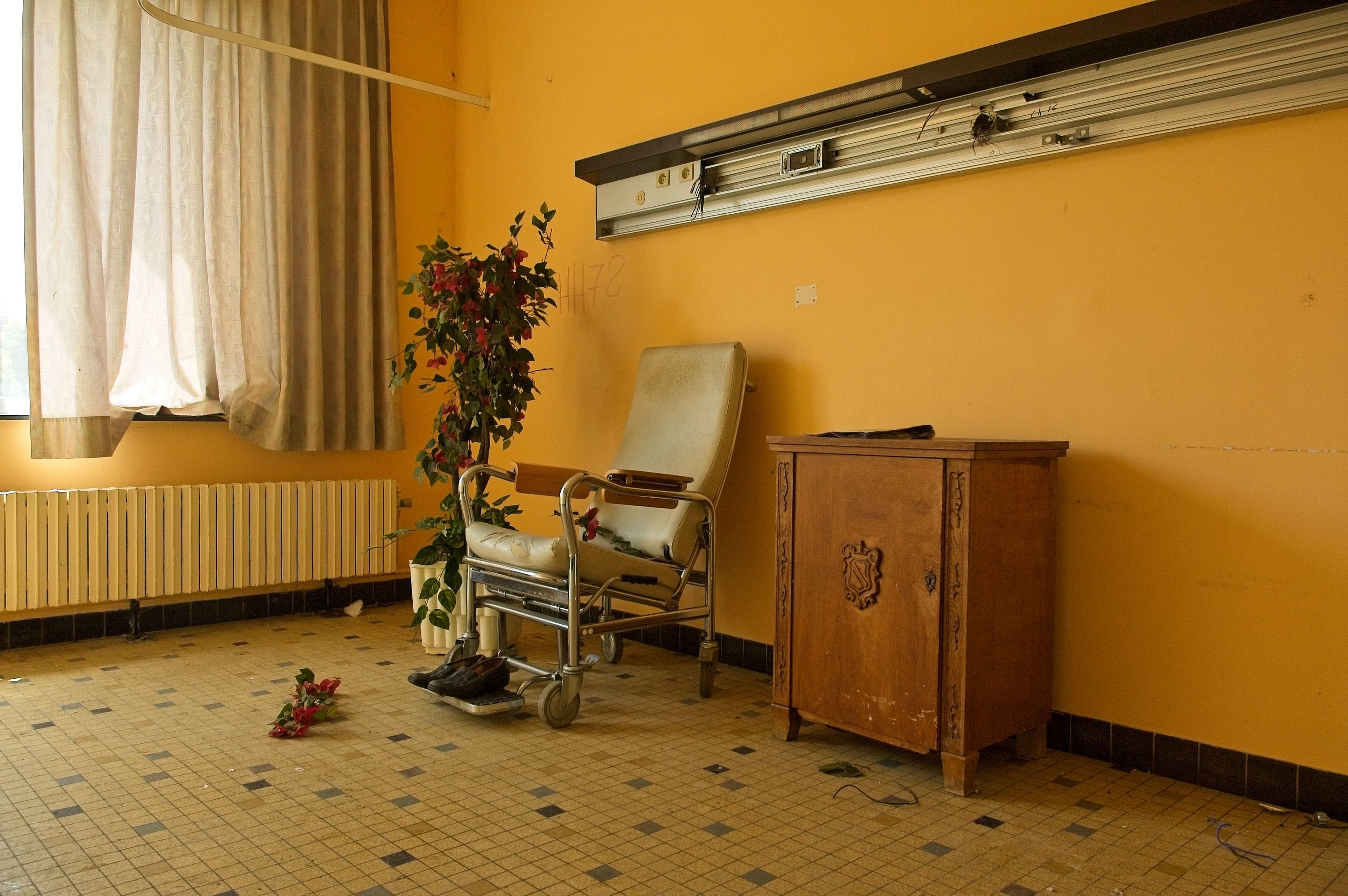 An old hospital room with a wheelchair, cabinet and scattered shoes