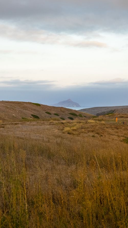 Free Calm and scenic coastal landscape with hills and a distant island visible under a soft sky. Stock Photo
