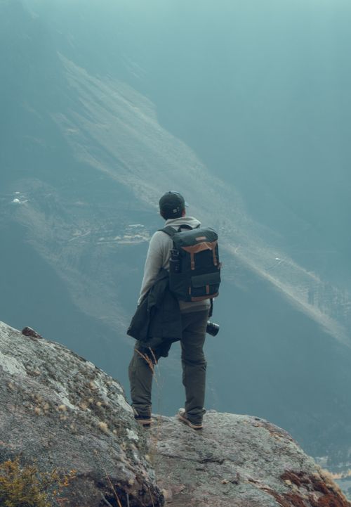 Free Explorer with backpack standing on a mountain edge, embracing adventure and nature. Stock Photo