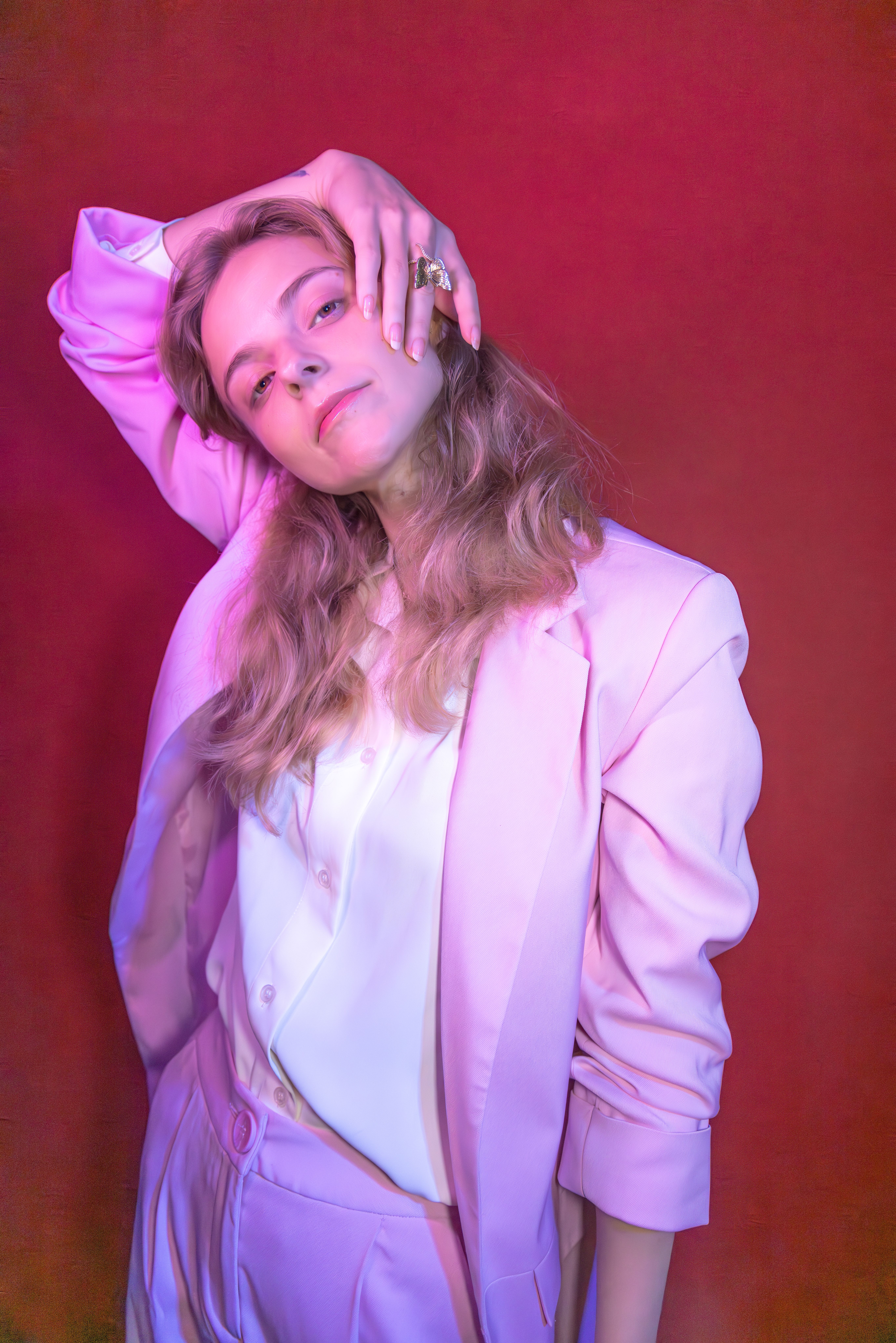 Creative portrait of a blonde woman in a pink suit posing gracefully against a vibrant backdrop.