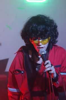 Dynamic image of a singer with curly hair and sunglasses on stage.