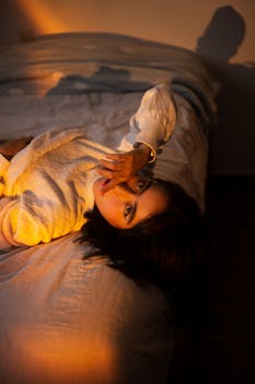 A woman in white clothes lying on bed with warm sunlight creating a dramatic effect.