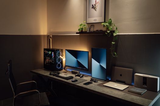 A sleek and modern desk setup featuring dual monitors, gaming PC, and tech gadgets in a well-lit room.