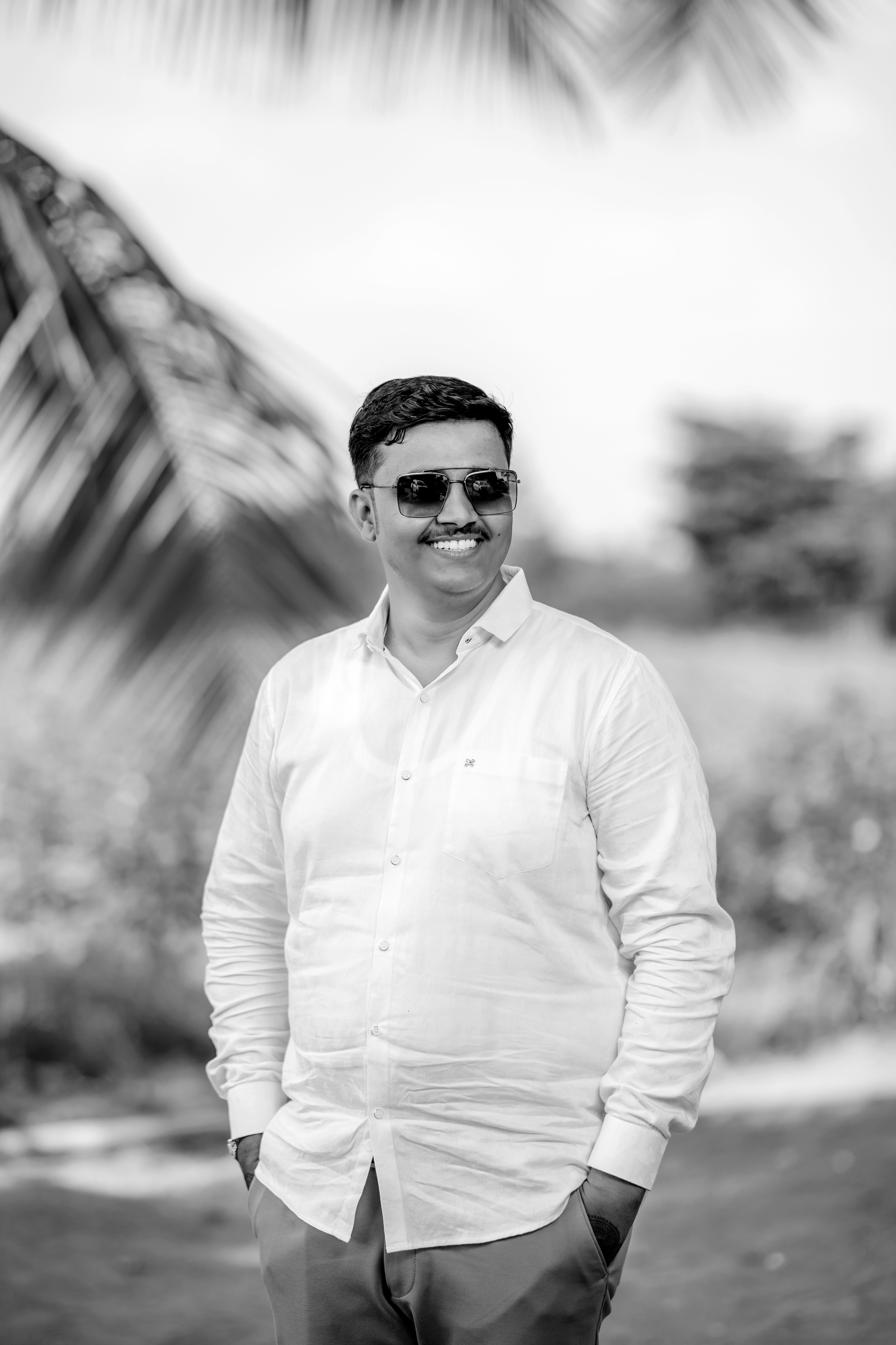 Black and white portrait of a smiling man in sunglasses, standing outdoors.