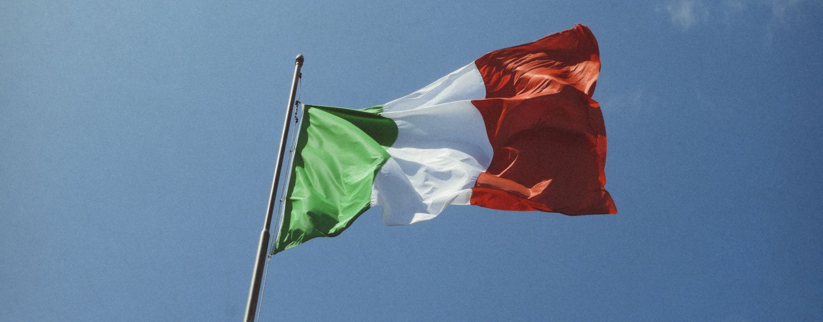 Low angle shot of the Italian flag waving against a clear blue sky.