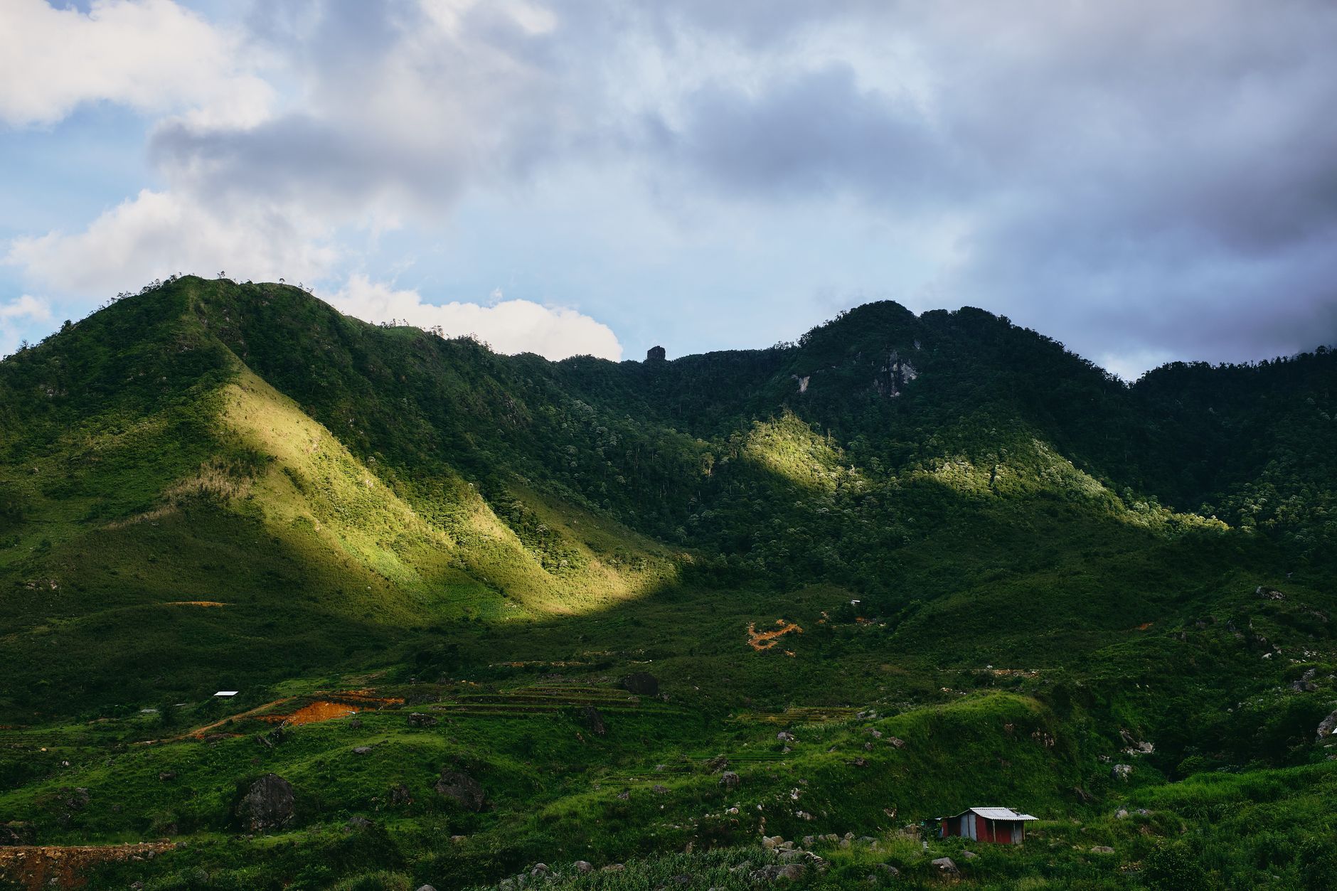 Breathtaking aerial view of lush green hills and valleys in Lào Cai, Vietnam, under a cloudy blue sky.