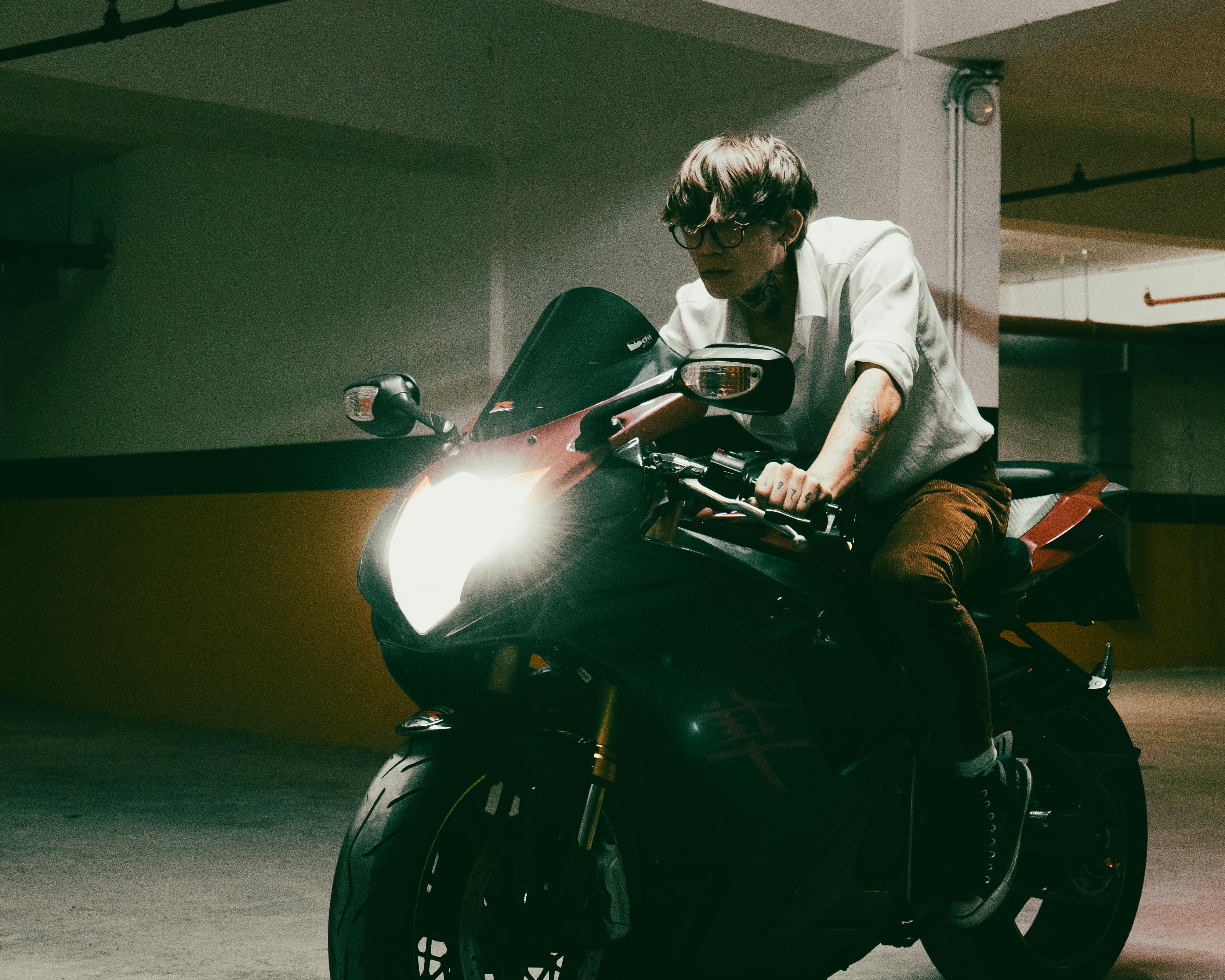Free A man on a motorcycle in a dimly lit parking garage with headlight on, creating a dramatic atmosphere. Stock Photo