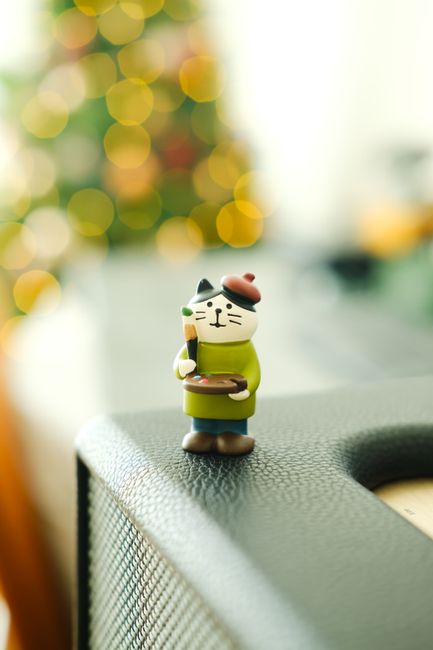 Whimsical cat figurine on speaker with bokeh Christmas lights in background, creating a festive atmosphere.