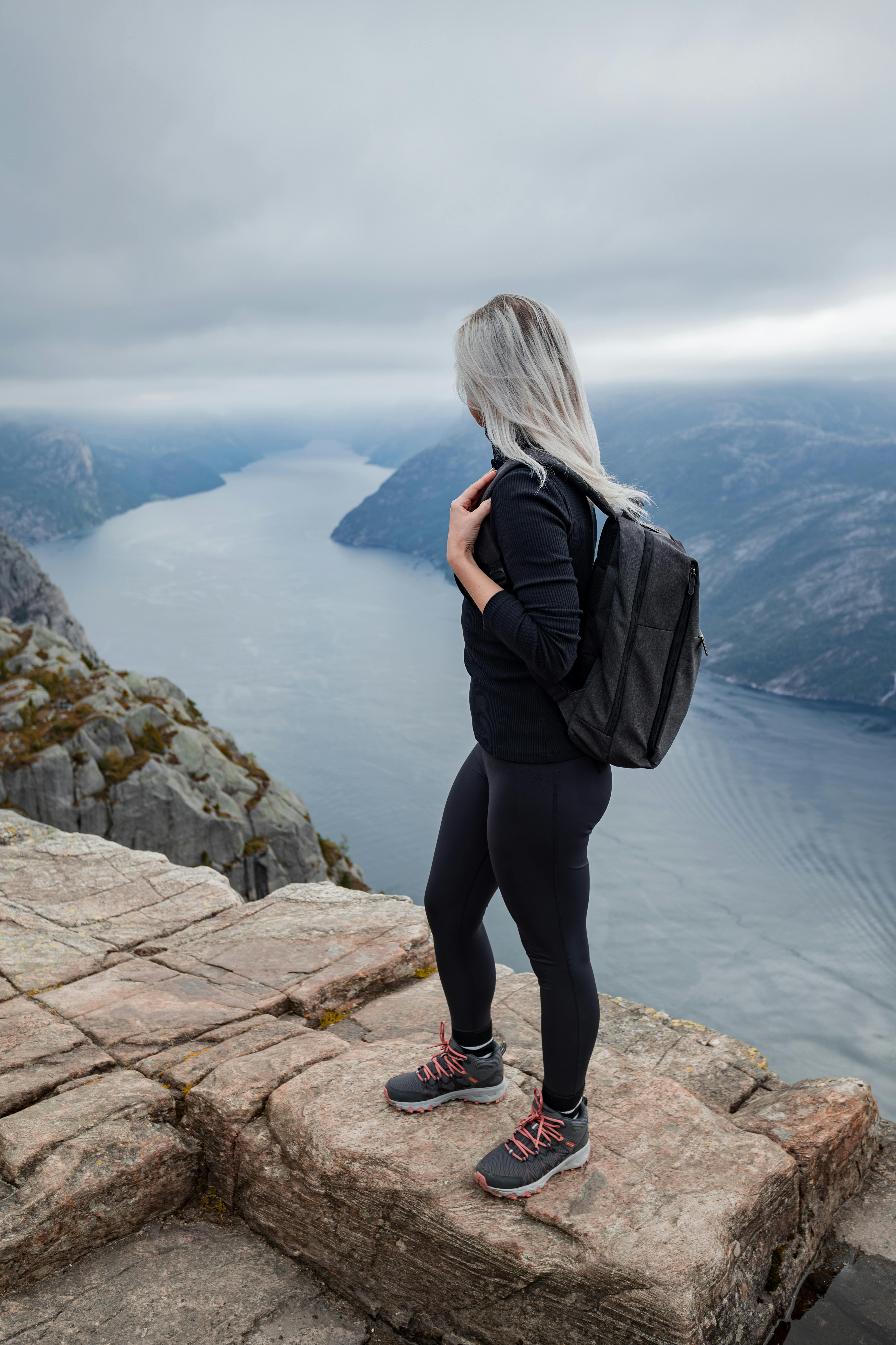 Woman hiker with backpack overlooking scenic Norwegian fjord from a stone cliff.