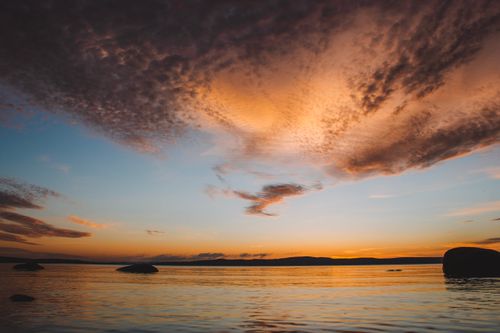 Free Vibrant sunset casting orange hues over a calm ocean with dramatic clouds. Stock Photo