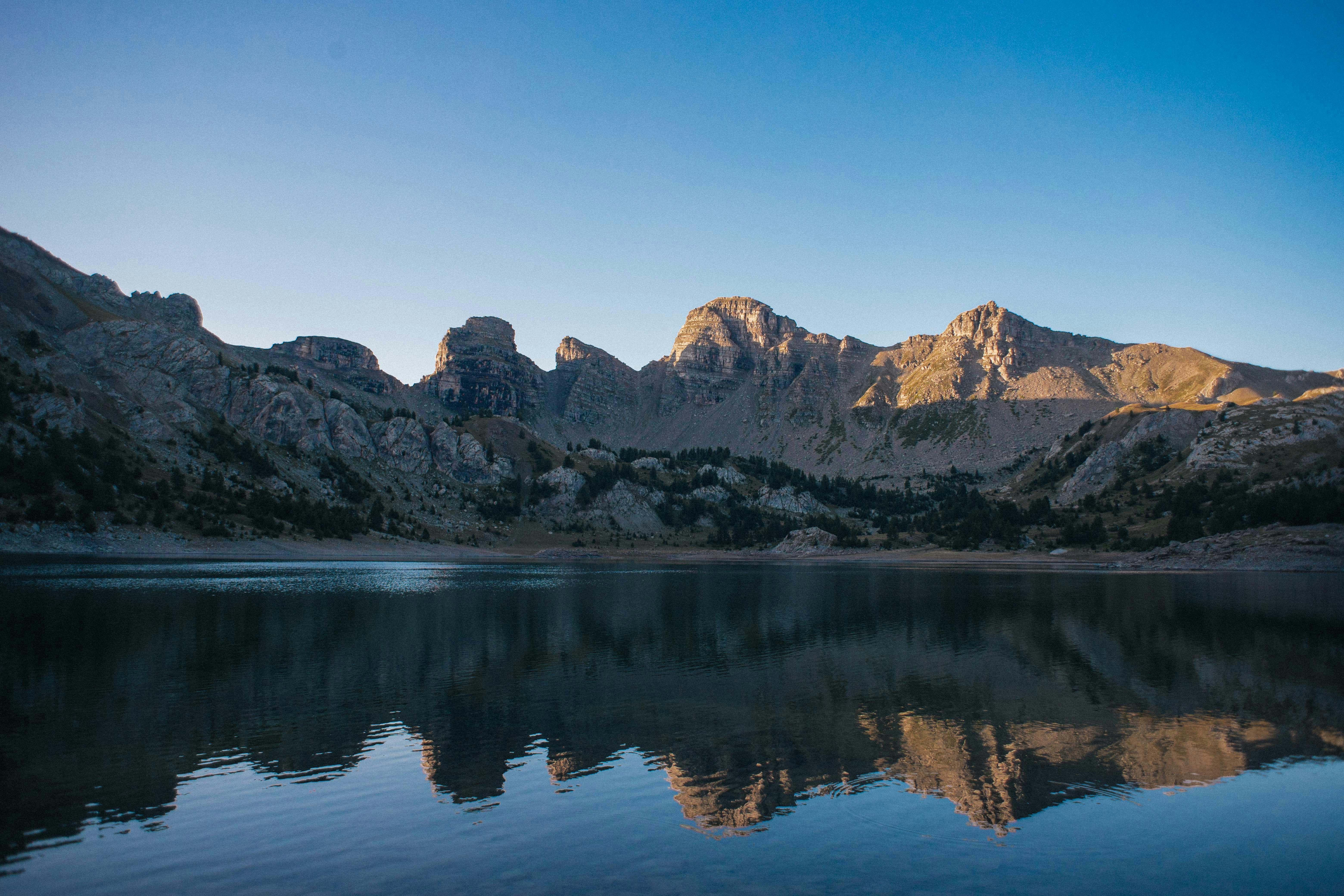 Tranquil lake reflecting mountains at sunrise in Allos, France, capturing serene natural beauty.
