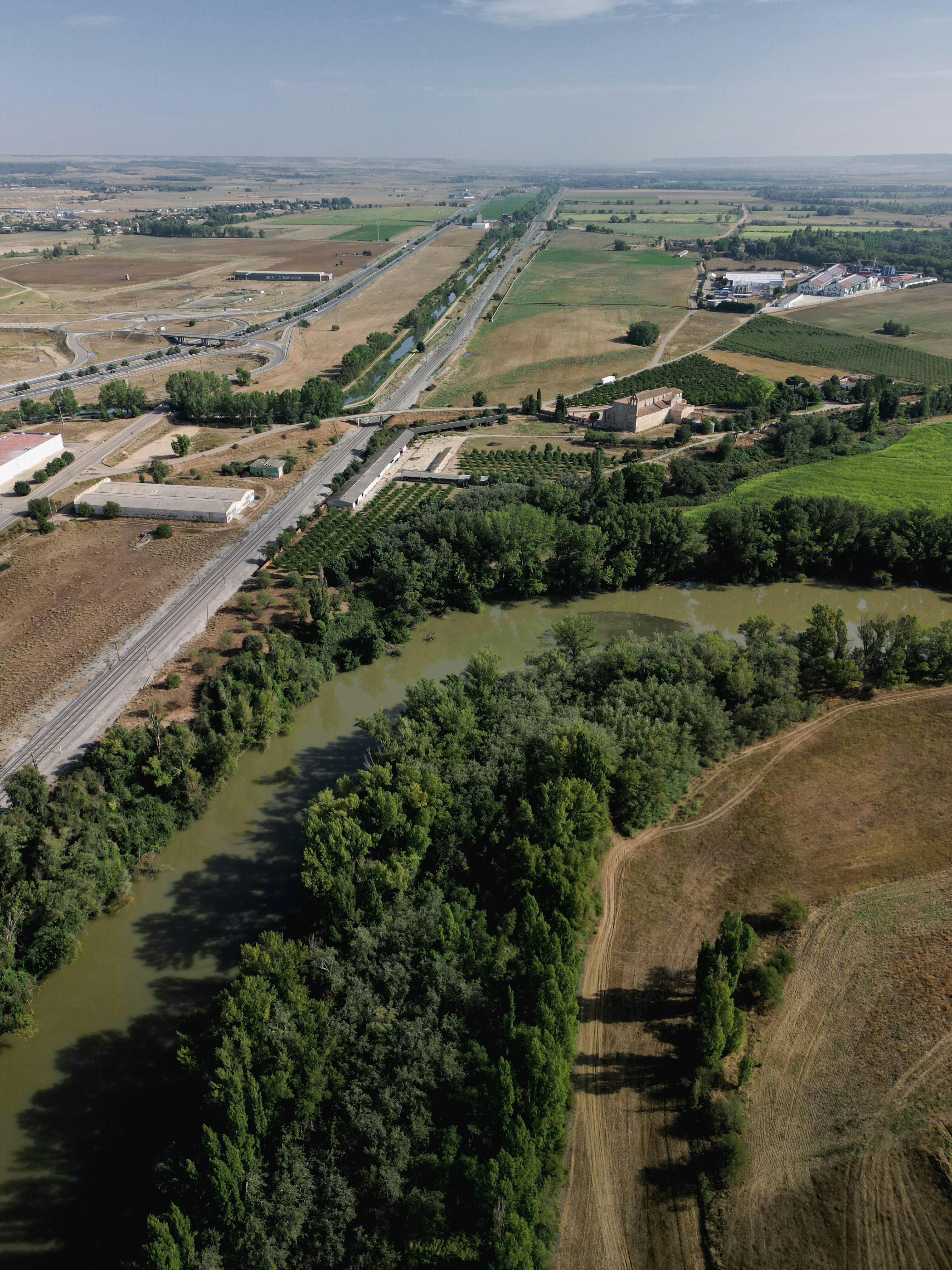 Aerial view of a lush landscape with a river, fields, and a highway under a clear sky. Ideal for nature and travel themes.